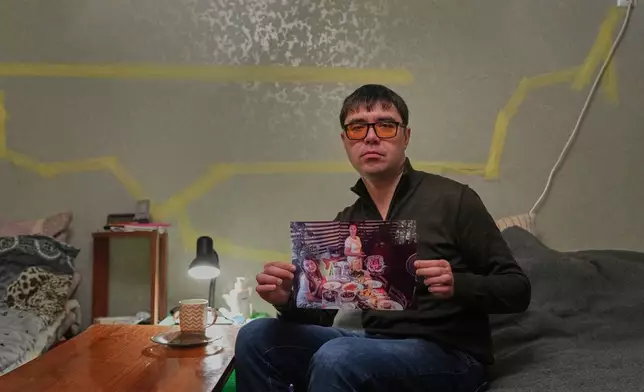 Yaroslav Nehoda, 40, holds a photograph of his niece, from left, wife and daughter, who were killed in a Russian drone attack on their house, as he sits in the temporary home he's living in, Thursday, Feb. 19, 2026, in Kyiv region, Ukraine. (AP Photo/Sergei Grits)