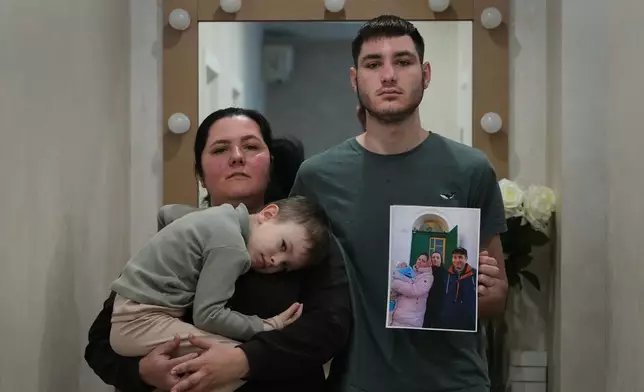 Oksana Osypenko, 43, her sons Davyd, right, and Hlib, 5, pose with a photograph, Thursday, Feb. 19, 2026, in Kyiv, Ukraine, taken before Russia's full-scale invasion showing her husband, Oleksandr, who was killed in an airstrike. (AP Photo/Sergei Grits)