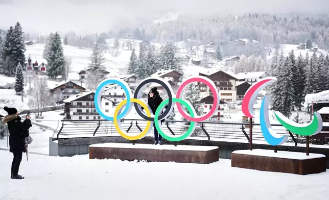 FILE - People take photos in front of the Milan Cortina Winter Olympics and Paralympics rings, in Cortina D'Ampezzo, Nov. 20, 2025. (AP Photo/Andrew Medichini, File)