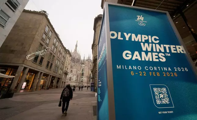 FILE - People walk along the Corso Vittorio Emanuele II, the main downtown street, near a sign for the upcoming Milan-Cortina Winter Olympics in Milan, Italy, Jan. 9, 2026. (AP Photo/Luca Bruno, File)