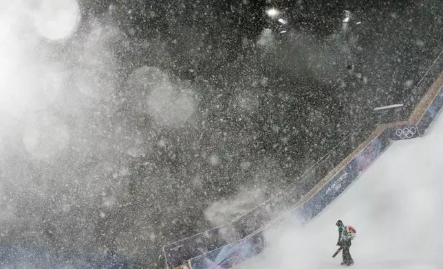 A worker blows snow off the course during heavy snow before the women's freestyle skiing big air finals at the 2026 Winter Olympics, in Livigno, Italy, Monday, Feb. 16, 2026. (AP Photo/Abbie Parr)