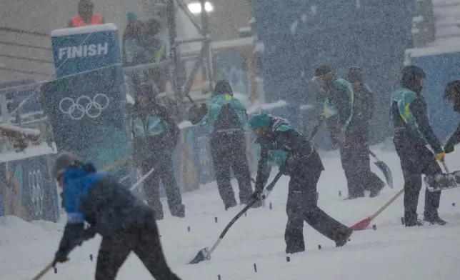 Volunteers remove snow on the finish area before the Biathlon Men's 4 x 7.5km Relay at the 2026 Winter Olympics, in Anterselva, Italy, Tuesday, Feb. 17, 2026. (AP Photo/Christophe Ena)