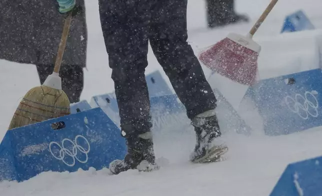 Workers remove snow on the finish area before the Biathlon Men's 4 x 7.5km Relay at the 2026 Winter Olympics, in Anterselva, Italy, Tuesday, Feb. 17, 2026. (AP Photo/Christophe Ena)
