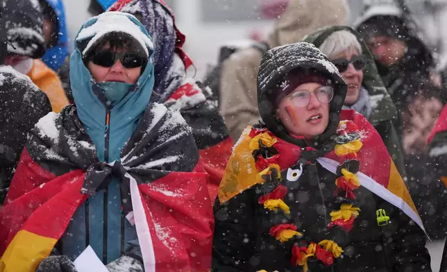 Fans for Germany's Emma Weiss brave heavy snow during a weather delay before the women's freestyle skiing aerials qualifications at the 2026 Winter Olympics, in Livigno, Italy, Tuesday, Feb. 17, 2026. (AP Photo/Gregory Bull)