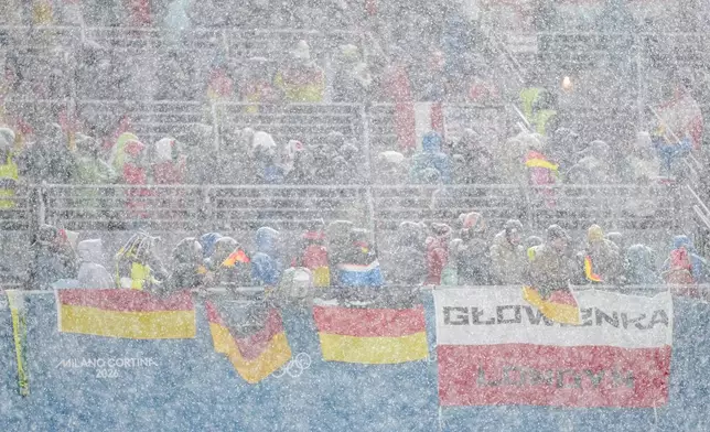 Germany and Poland fans on the stands wait while a snowfall interrupts the final round jump of the ski jumping men's super team competition at the 2026 Winter Olympics, in Predazzo, Italy, Monday, Feb. 16, 2026. (AP Photo/Matthias Schrader)