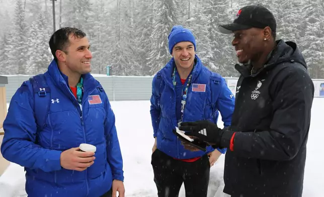 United States' bobsledders Frank Del Duca, left and Boone Niederhofer speak with De Aundre John, right, a bobsledder from Trinidad and Tobago after trading their unique national team pins, at the Cortina Olympic Village, during the 2026 Winter Olympics, in Cortina d'Ampezzo, Italy, Tuesday, Feb. 3, 2026. (AP Photo/Jennifer McDermott)