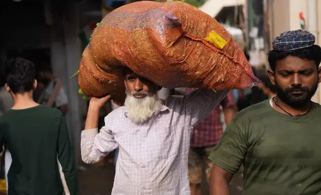 A vegetable vendor carries a sack of vegetables at a local market in Mumbai, India, Sunday, Feb. 1, 2026. (AP Photo/Rafiq Maqbool)