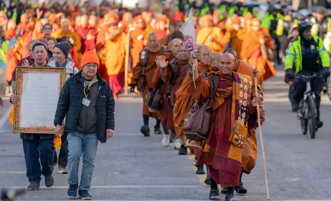 Monk Bhikkhu Pannakara waves to the crowd as he walks along with Buddhist monks who are participating in a Walk For Peace walk through a the streets of Washington, Tuesday, Feb. 10, 2026, (AP Photo/Jose Luis Magana)