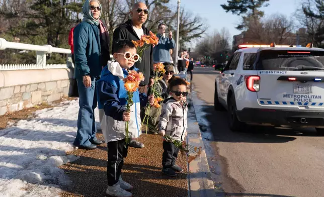People holding flowers watch the Buddhist monks who are participating in a Walk For Peace walk through a the streets of Washington, Tuesday, Feb. 10, 2026. (AP Photo/Jose Luis Magana)