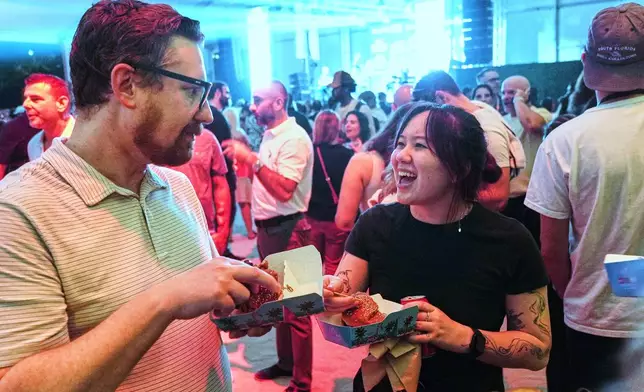 A couple enjoys the Burger Bash at the South Beach Wine and Food Festival Friday, Feb. 20, 2026, in Miami Beach, Fla. (AP Photo/Marta Lavandier)