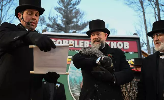 Groundhog Club Vice President Dan McGinley reads the scroll as handler A.J. Dereume holds Punxsutawney Phil, the weather prognosticating groundhog, during the 140th celebration of Groundhog Day on Gobbler's Knob in Punxsutawney, Pa., Monday, Feb. 2, 2026, Phil's handlers said that the groundhog has forecast six more weeks of winter. (AP Photo/Barry Reeger)