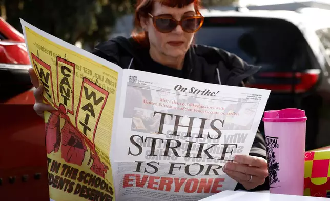 Bret Harte Elementary Stacey Gonzalez TK teacher reads a United Educators of San Francisco newspaper as Bret Harte Elementary School teachers and Untied Educators of San Francisco members strike outside of Bret Harte Elementary School in San Francisco, Calif., Tuesday, Feb. 10, 2026. (Jessica Christian/San Francisco Chronicle via AP)
