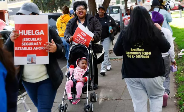 Bret Harte Elementary kindergarten to second grade teacher Kalina Francois pushes her daughter Inayah, 1, in a stroller while joining Bret Harte Elementary School teachers and Untied Educators of San Francisco members in a strike outside of Bret Harte Elementary School in San Francisco, Calif., Tuesday, Feb. 10, 2026. (Jessica Christian/San Francisco Chronicle via AP)