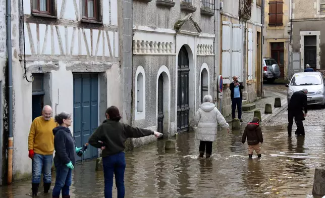 People walk in a flooded street of Confolens as severe flooding hits western France amid storm Nils, Thursday, Feb. 12, 2026. (AP Photo/Yohan Bonnet)