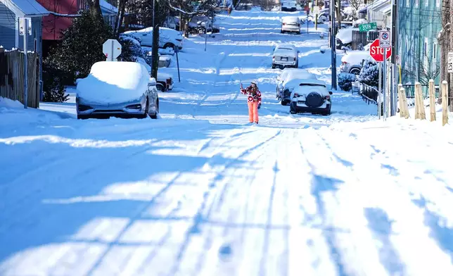 A woman takes a photo on a snow-covered street, Sunday, Feb 1, 2026, in Charlotte, N.C. (AP Photo/Matt Kelley)