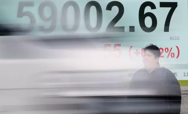 A person stands as a vehicle passes by in front of an electronic stock board showing Japan's Nikkei index at a securities firm Thursday, Feb. 26, 2026, in Tokyo. (AP Photo/Eugene Hoshiko)