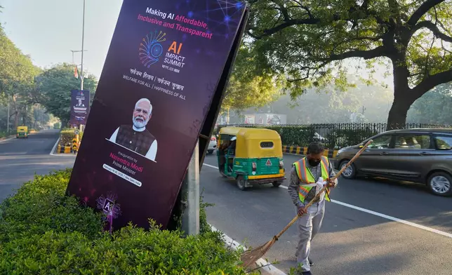 A municipal worker sweeps on a street with banners of the AI-Summit with Indian Prime Minister Narendra Modi photographs in New Delhi, India, Monday, Feb. 16, 2026. (AP Photo/Manish Swarup)