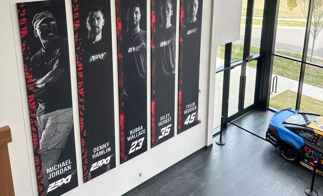 A banner, showing co-owners Michael Jordan and Denny Hamlin, as well as drivers Bubba Wallace, Corey Heim and Tyler Reddick, hangs in the lobby at Airspeed, the headquarters of 23XI Racing, Tuesday, Feb. 24, 2026 in Huntersville, N.C. (AP Photo/Jenna Fryer)