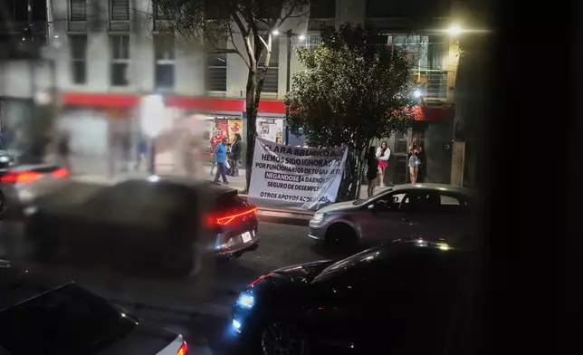 Photographed through a window on the metro, a sign directed at Mexico City Mayor Clara Brugada protests a new bike lane being built by the city along Calzada de Tlalpan in preparation for the World Cup, because it blocks cars from pulling over and cuts into the livelihoods of sex workers and street vendors, in Mexico City, Monday, Feb. 9, 2026. (AP Photo/Eduardo Verdugo)
