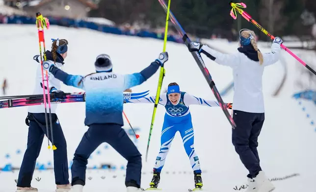 Jasmi Joensuu, of Finland, approaches the finish line and celebrating teammates to win the bronze medal in the cross country skiing women's 4 x 7.5km relay at the 2026 Winter Olympics, in Tesero, Italy, Saturday, Feb. 14, 2026. (AP Photo/Matthias Schrader)