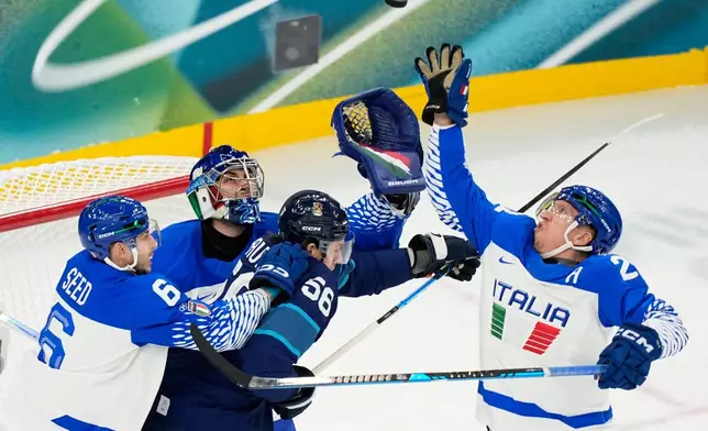 Italy's goalkeeper Damian Clara, center, and Italy's Diego Kostner, right, reach for the puck during a preliminary round match of men's ice hockey between Finland and Italy at the 2026 Winter Olympics, in Milan, Italy, Saturday, Feb. 14, 2026. (AP Photo/Hassan Ammar)