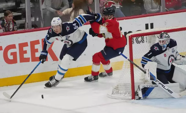 Winnipeg Jets defenseman Logan Stanley (64) takes control of the puck from Florida Panthers left wing A.J. Greer (10) during the third period of an NHL hockey game, Saturday, Jan. 31, 2026, in Sunrise, Fla. (AP Photo/Marta Lavandier)