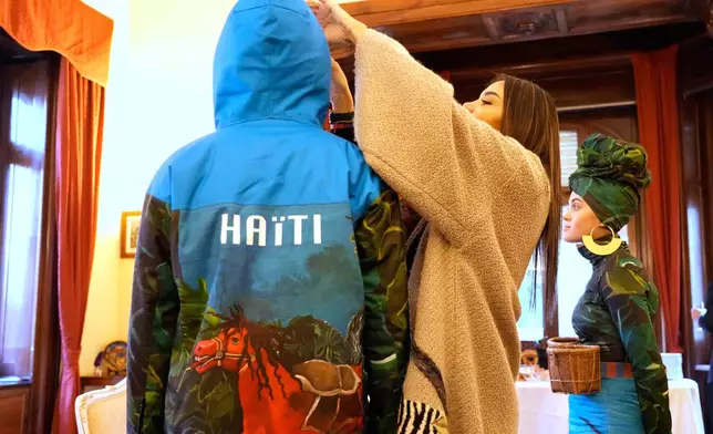 Italian-Haitian designer Stella Jean, center, helps Megan Thomas, left, and Livia Audain at the Haitian Embassy in Rome, Saturday, Jan. 31, 2026, wear the official uniform of the Haitian national team participating in the 2026 Winter Olympics. (AP Photo/Gregorio Borgia)