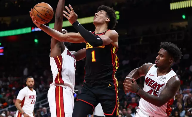 Atlanta Hawks forward Jalen Johnson (1) shoots against Miami Heat center Bam Adebayo, left, and guard Davion Mitchell, right, during the first half of an NBA basketball game, Friday, Feb. 20, 2026, in Atlanta. (AP Photo/Colin Hubbard)