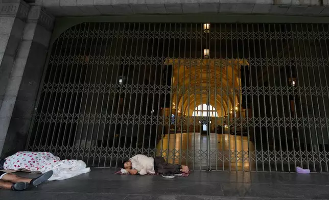 People sleep near the closed entrances of Constitucion railway station during a union strike against a proposed labor reform bill in Buenos Aires, Argentina, Thursday, Feb. 19, 2026. (AP Photo/Gustavo Garello)