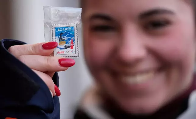 A woman shows a pin she is looking to trade at the 2026 Winter Olympics, in Cortina d'Ampezzo, Italy, Wednesday, Feb. 11, 2026. (AP Photo/Robert F. Bukaty)