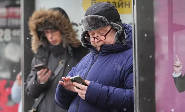 People look at their smartphones at a bus stop in St. Petersburg, Russia, Wednesday, Feb. 11, 2026. (AP Photo/Dmitri Lovetsky)