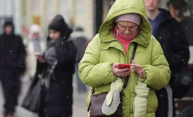 A woman looks at her smartphone at a bus stop in St. Petersburg, Russia, Wednesday, Feb. 11, 2026. (AP Photo/Dmitri Lovetsky)