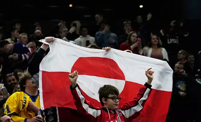 Fans hold Greenland national flag before a preliminary round match of men's ice hockey between United States and Denmark at the 2026 Winter Olympics, in Milan, Italy, Saturday, Feb. 14, 2026. (AP Photo/Petr David Josek)