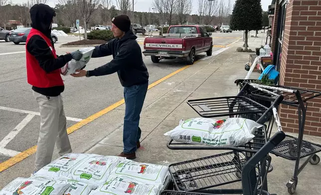Hunter Steffen, 17, left, hands a hard-to-come by 40-pound bag of ice melt to a customer outside Town &amp; County Hardware in Wake Forest, N.C., on Saturday, Jan. 31, 2026. (AP Photo/Allen G. Breed)