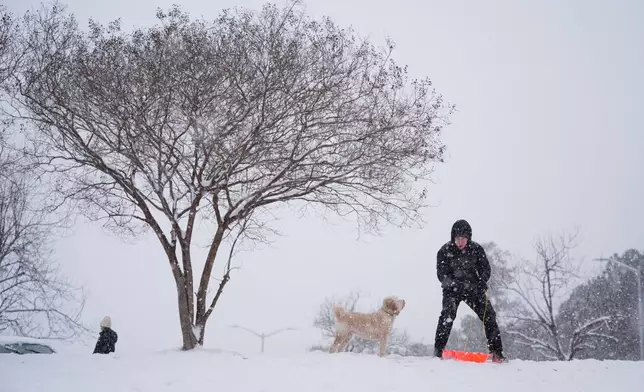 Alex Taylor, accompanied by his dog Daisy, prepared to slide down a snow-covered hill in Charlotte, N.C., Saturday, Jan. 31, 2026. (AP Photo/Erik Verduzco)