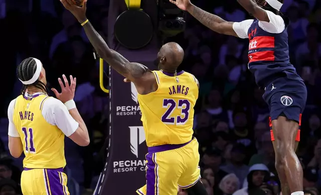Los Angeles Lakers forward LeBron James, center, shoots against Washington Wizards guard Bub Carrington, right, as forward Jaxson Hayes watches during the first half of an NBA basketball game Monday, March 30, 2026, in Los Angeles. (AP Photo/Ryan Sun)