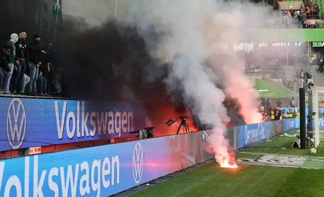 Wolfsburg fans throw flares onto the pitch following the German Bundesliga soccer match between Hamburger and Wolfsburg in Wolfsburg, Germany, Saturday, March 7, 2026. (Andreas Gora/dpa via AP)
