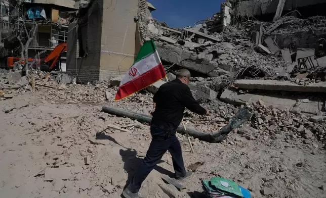 A man carries an Iranian flag to place on the rubble of a police facility struck during the U.S.–Israeli military campaign in Tehran, Iran, Wednesday, March 4, 2026. (AP Photo/Vahid Salemi)