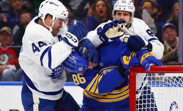 Buffalo Sabres center Noah Ostlund (86) is grabbed by Toronto Maple Leafs defenseman Morgan Rielly (44) and defenseman Oliver Ekman-Larsson (95) during the first period of an NHL hockey game Saturday, March 14, 2026, in Buffalo, N.Y. (AP Photo/Jeffrey T. Barnes)