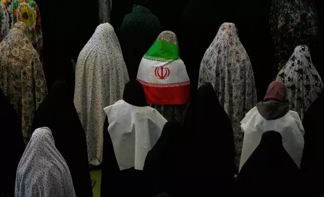 Iranian worshippers perform Eid al-Fitr prayers marking the end of the holy fasting month of Ramadan as one of them wears an Iranian flag at the Imam Khomeini Grand Mosque in Tehran, Iran, Saturday, March 21, 2026. (AP Photo/Vahid Salemi)
