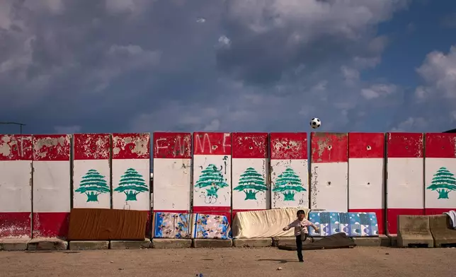A boy, displaced with his family from Beirut's southern suburbs of Dahiyeh, plays with a ball next to rain-soaked mattresses drying in the sun in Beirut, Lebanon, Friday, March 27, 2026. (AP Photo/Emilio Morenatti)