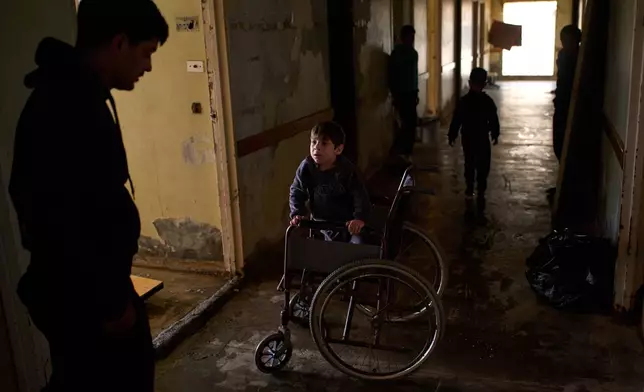 Abbas, 5, who suffers from a genetic condition that prevents him from walking, speaks with his father in a hallway of a hospital converted into a shelter in Beirut, Lebanon, Friday, March 27, 2026, after they were displaced from Dahiyeh, Beirut's southern suburbs. (AP Photo/Emilio Morenatti)