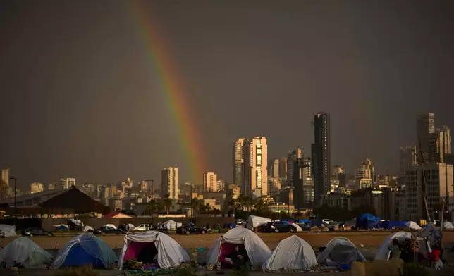 Displaced people who fled Israeli strikes in southern Lebanon sit inside tents used as shelters as a rainbow breaks through the rain in Beirut, Lebanon, Sunday, March 29, 2026. (AP Photo/Emilio Morenatti)
