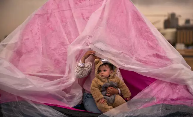 Yasmin holds her brother Ali, both displaced from Beirut's southern suburb of Dahiyeh, as they shelter from the rain inside a tent along the coast in Beirut, Lebanon, Thursday, March 26, 2026. (AP Photo/Emilio Morenatti)