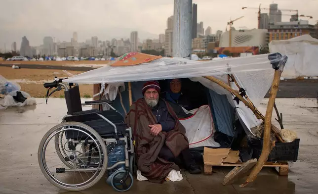 A man with his wife, displaced from Beirut's southern suburb of Dahiyeh, shelter from the rain inside a tent along the coast in Beirut, Lebanon, Thursday, March 26, 2026. (AP Photo/Emilio Morenatti)