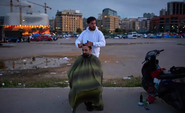 Hussein gets a haircut from Hassan in an open field where people who fled Israeli strikes in southern Lebanon have set up tents as shelters, in Beirut, Lebanon, Wednesday, March 25, 2026. (AP Photo/Emilio Morenatti)