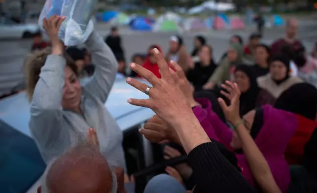 Displaced women reach out to receive an aid package distributed by a volunteer in Beirut, Lebanon, Friday, March 27, 2026. (AP Photo/Emilio Morenatti)
