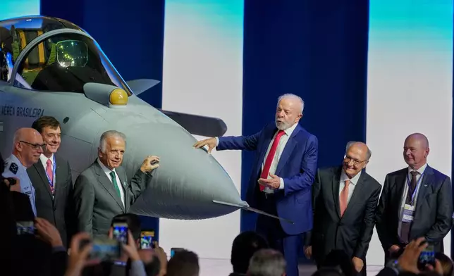Brazilian President Luiz Inacio Lula da Silva, center, stands next to an F-39E Gripen fighter jet during a ceremony presenting the first supersonic aircraft assembled in Brazil, developed by Saab, at the Embraer plant in Gaviao Peixoto, Brazil, Wednesday, March 25, 2026. From left are Brazilian Air Force Commander Marcelo Kanitz Damasceno, Embraer CEO Francisco Gomes Neto, Defense Minister Jose Mucio, Lula, Vice President Geraldo Alckmin, and Saab CEO Micael Johansson. (AP Photo/Andre Penner)