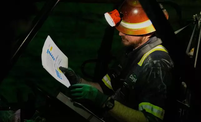 The absolute darkness of the mine is broken as supervisor Andrew Adkins uses a headlamp to lookover a map of drilling sites at the Cargill Salt Mine, 1,800 feet below the surface of Lake Erie, in Cleveland, Ohio, Thursday, March 19, 2026. (AP Photo/Sue Ogrocki)