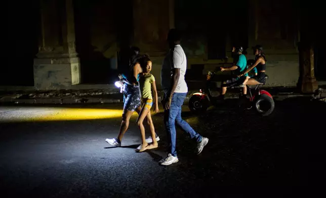 People walk on a street during a blackout in Havana, Monday, March 16, 2026. (AP Photo/Ramon Espinosa)